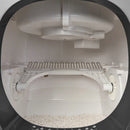 Innenansicht in die Cat Mate automatische Katzentoilette, die den selbstreinigenden Mechanismus mit einem weißen rotierenden Reinigungsrechen zeigt, der auf zylindrischen Rollen montiert ist. Der Rechen verfügt über gebogene Metallzinken, die entwickelt wurden, um durch Streu zu sieben. Darüber befindet sich ein weißes Streuausgabesystem mit mehreren Fächern. Frische klumpende Streu ist am Boden der weißen Kammer sichtbar, durch die abgerundete Eingangsöffnung betrachtet, die von einem schwarzen Rand einger